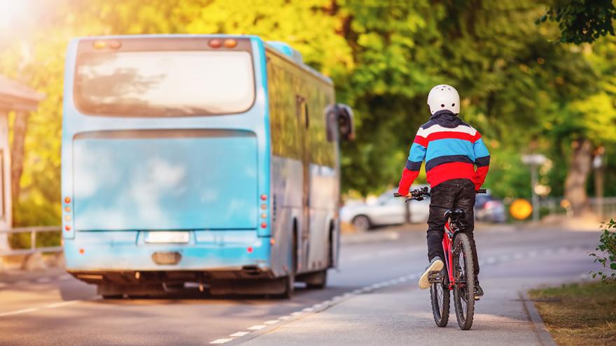 Kind fährt auf Fahrrad hinter einem Bus her